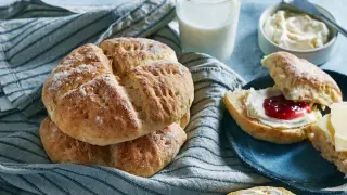 En hög med söta scones, redo att avnjutas med sylt och grädde. Ett glas mjölk står bredvid, perfekt för en mysig fika.
