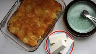 En gyllene bananpaj i en glasform, bredvid en hög med tallrikar och en liten tallrik med bitar av vit choklad.