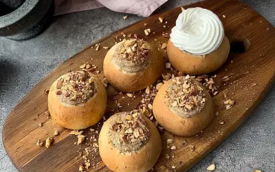 Färdiga semlor med mandelmassa till, toppade med hackade nötter och en generös klick grädde på en av dem.