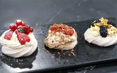 Tre små pavlovakakor med olika toppingar: jordgubbar och vinbär, choklad och hallon, samt björnbär och pistagenötter.