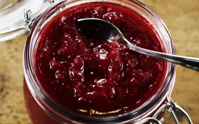 En burk med hemgjord lingonsylt, perfekt för ett enkelt lingonsylt recept. En sked vilar i den rika, röda sylten.