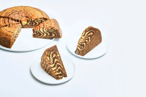 A sliced zebra cake with a marbled chocolate and vanilla pattern, served on white plates.