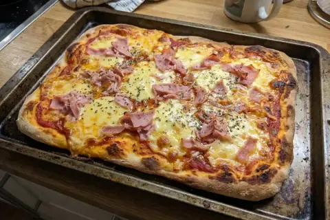 En nybakad pizza med skinka och ost på en plåt. Perfekt för en snabb middag med snabb pizzadeg!