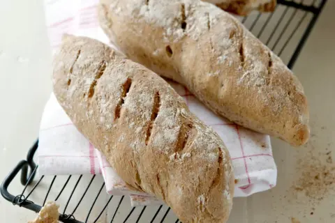 Två nybakade bröd, perfekta för ett skrädmjöl recept. Ligger på ett rutigt tyg på ett galler.