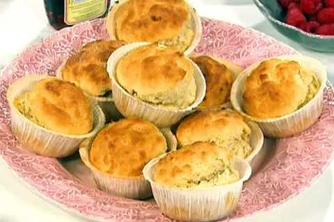 En rosa bricka med nybakade dinkelscones i pappersformar. Bredvid syns hallon och en burk sylt.