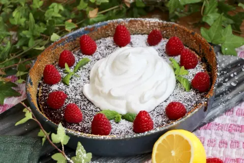 Chokladpaj med hallon och fluffig vegansk filmjölk, pudrad med florsocker. En citronskiva ligger bredvid.