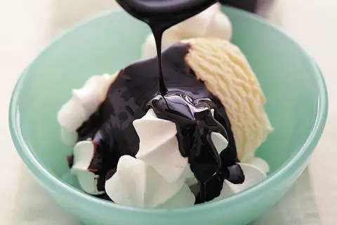 En skopa vaniljglass med vispgrädde och mörk chokladsås som hälls över. Perfekt för ett enkelt chokladsås recept.