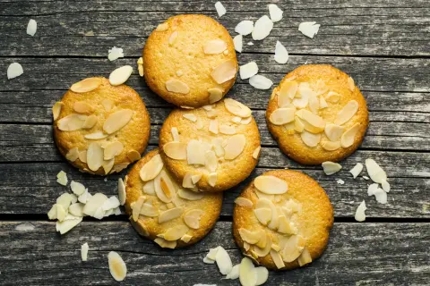 Små, gyllene mandelkakor, perfekta för ett bondkakor recept. Spridda mandelflagor på en rustik träyta.