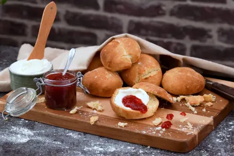 Färska scones havregryn med sylt och grädde på en träskärbräda.