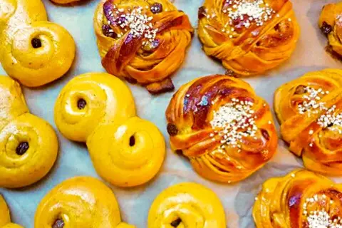 En närbild av saftiga lussebullar, vissa med russin och pärlsocker, andra med enbart russin. De ser otroligt goda ut!