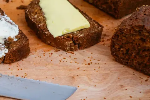 Mörkt bröd med smör och en skiva med yoghurt på en skärbräda.