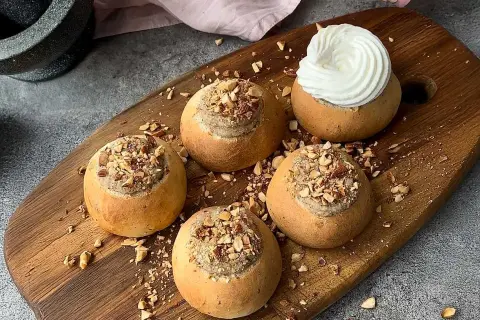Färdiga semlor med mandelmassa till, toppade med hackade nötter och en generös klick grädde på en av dem.