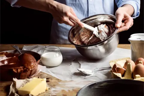 Händer blandar chokladsmet i skål. Ingredienser som smör, ägg och mjölkfri filmjölk ligger framme.