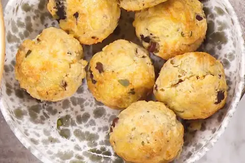 En skål med matiga scones, gyllene och med mörka bitar av oliver eller soltorkade tomater. Perfekta för en rejäl fika.