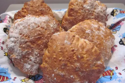 Nybakade scones med yoghurt, pudrade med mjöl, ligger i en korg med ett färgglatt mönster.