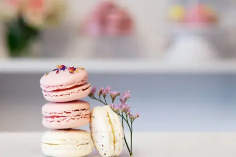 En stapel rosa och vita macarons, dekorerade med blomblad. Ett enkelt macarons recept för en vacker dessert.