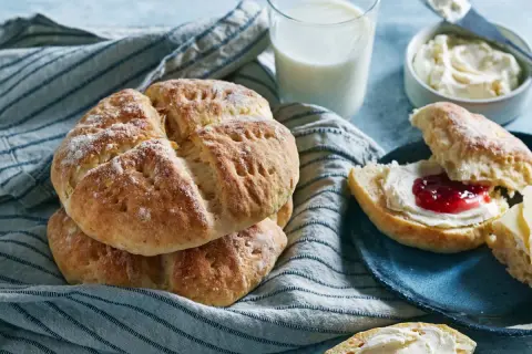 En hög med söta scones, redo att avnjutas med sylt och grädde. Ett glas mjölk står bredvid, perfekt för en mysig fika.