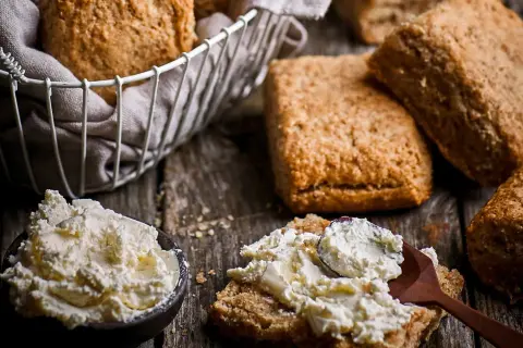 Scones med grahamsmjöl serveras med en skål krämig ost och en sked som sprider den på en scone.