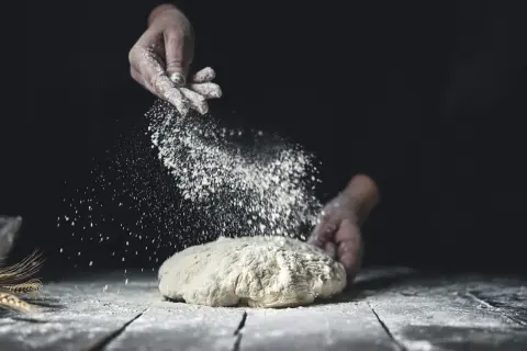 Händer strör mjöl över deg. Jämförelse mellan dinkelmjöl vs vetemjöl i bakning.