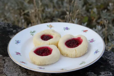 Tre glutenfria hallongrottor med sylt på en blommig tallrik.