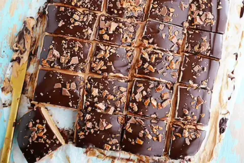 Biskvier i långpanna med chokladglasyr och krossad toffee. En gyllene kniv ligger bredvid.