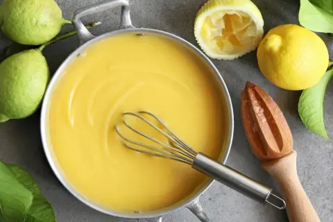 Kastrull med krämig lemon curd, färska citroner och en träpress. Perfekt för bakning!