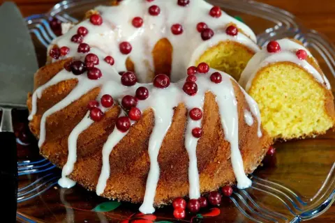 En gammaldags sockerkaka med glasyr och lingon. En bit är uppskuren och visar den gyllene insidan.