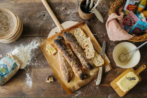 Nybakade surdegsbröd på en bakplåt, redo för ett gott surdeg recept. Ingredienser som mjöl och smör ligger utspridda.