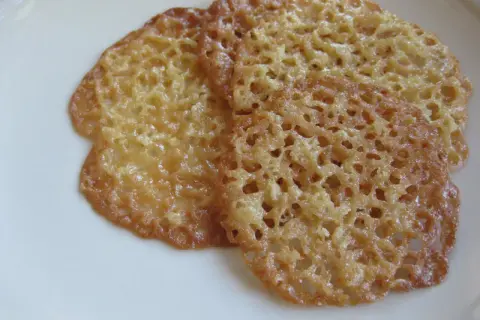 Tre gyllene havreflarn utan sirap ligger på en vit tallrik. De är tunna och krispiga med ett vackert nätmönster.