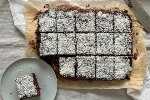 En plåt med chokladkakor, toppade med kokosflingor, redo att avnjutas som kärleksmums på påsk. En bit ligger på en tallrik.