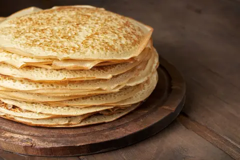 En hög med gyllene pannkakor på en träbricka, redo att frysa in pannkakor för framtida frukostar.