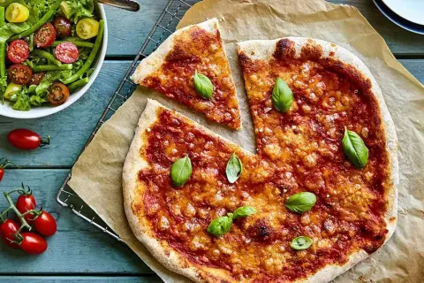 En hemmagjord pizza med nyttig pizzabotten, toppad med tomatsås och basilika. Bredvid en fräsch sallad med gröna bönor och tomater.
