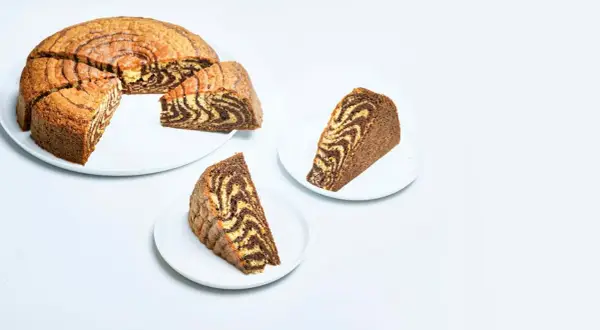 A sliced zebra cake with a marbled chocolate and vanilla pattern, served on white plates.