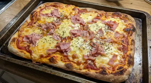 En nybakad pizza med skinka och ost på en plåt. Perfekt för en snabb middag med snabb pizzadeg!