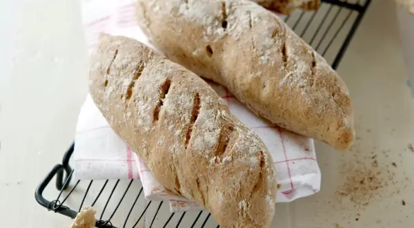 Två nybakade bröd, perfekta för ett skrädmjöl recept. Ligger på ett rutigt tyg på ett galler.