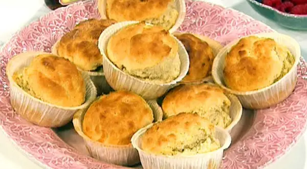 En rosa bricka med nybakade dinkelscones i pappersformar. Bredvid syns hallon och en burk sylt.