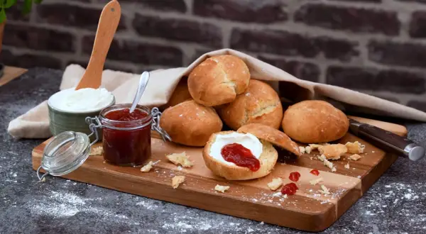 Färska scones havregryn med sylt och grädde på en träskärbräda.