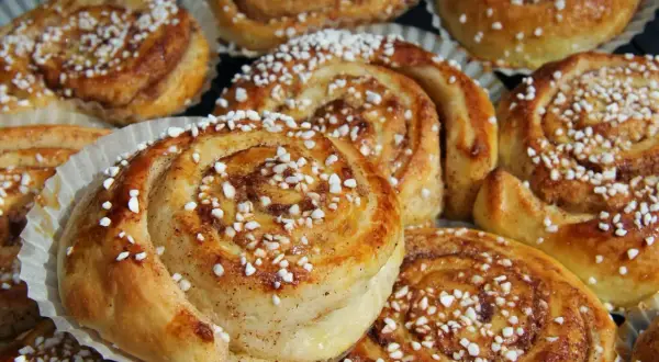 Nybakade kanelbullar med pärlsocker, redo att avnjutas. Doften av kanel och socker sprider sig från dessa gyllene tina frysta bullar i ugn.