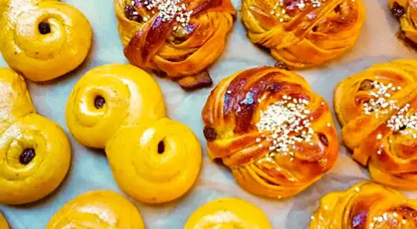 En närbild av saftiga lussebullar, vissa med russin och pärlsocker, andra med enbart russin. De ser otroligt goda ut!