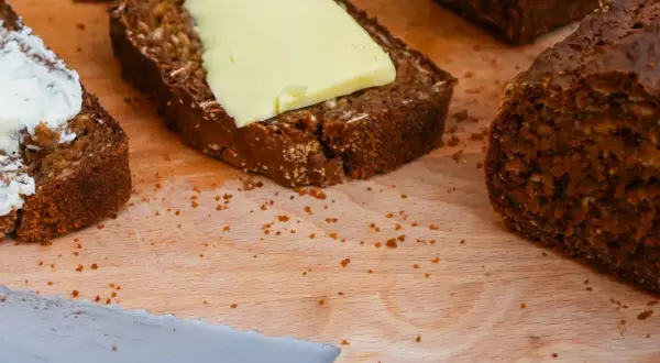 Mörkt bröd med smör och en skiva med yoghurt på en skärbräda.