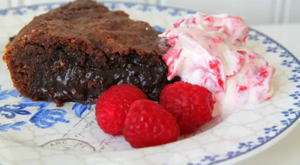 En bit kladdkaka med lakrits, serverad med hallon och grädde.