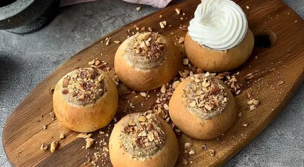 Färdiga semlor med mandelmassa till, toppade med hackade nötter och en generös klick grädde på en av dem.
