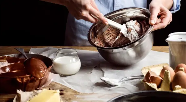 Händer blandar chokladsmet i skål. Ingredienser som smör, ägg och mjölkfri filmjölk ligger framme.