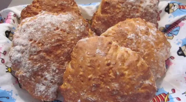 Nybakade scones med yoghurt, pudrade med mjöl, ligger i en korg med ett färgglatt mönster.