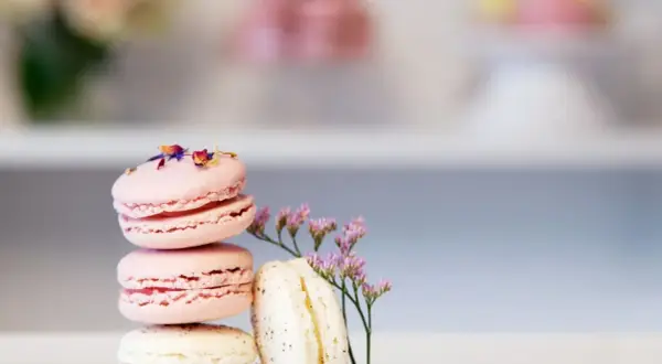 En stapel rosa och vita macarons, dekorerade med blomblad. Ett enkelt macarons recept för en vacker dessert.