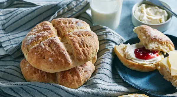 En hög med söta scones, redo att avnjutas med sylt och grädde. Ett glas mjölk står bredvid, perfekt för en mysig fika.