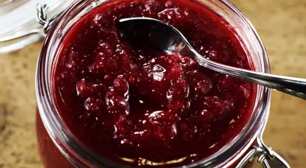 En burk med hemgjord lingonsylt, perfekt för ett enkelt lingonsylt recept. En sked vilar i den rika, röda sylten.
