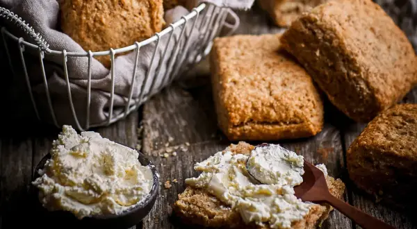 Scones med grahamsmjöl serveras med en skål krämig ost och en sked som sprider den på en scone.