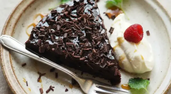 En bit kladdkaka toppad med chokladspån, serverad med vispad grädde, hallon och mynta. Perfekt för den som vill ha glutenfria kladdkakemuffins.