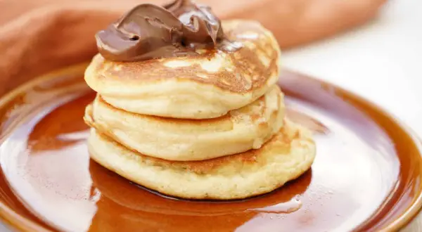 En hög med fluffiga american pancakes toppas med chokladkräm på en brun tallrik.